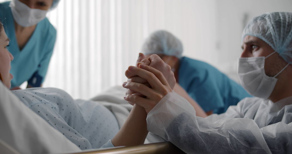 Man holding woman's hand during baby delivery.